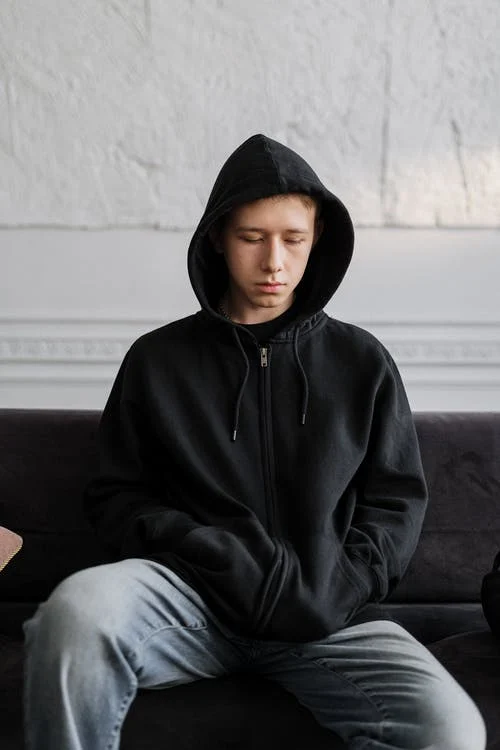 Male in black hoody looking at floor Tips For Looking After Your Well-Being